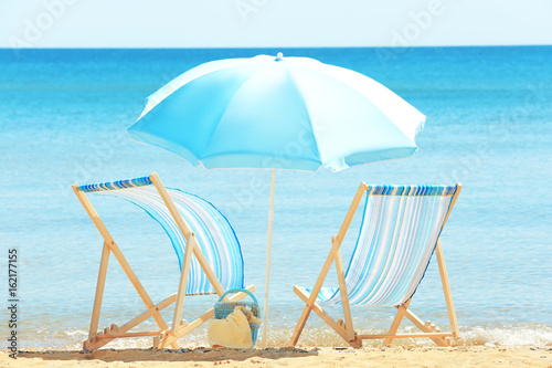 Pair of beach chairs and umbrella at sea shore. Vacation concept