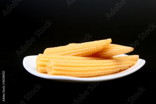 Mini Corn cob preserved on plate on wooden board. photo