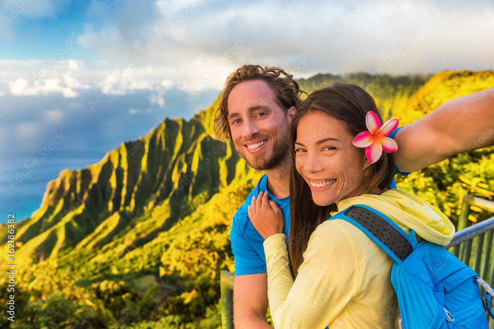 Na pali hikers couple tourists taking selfie at Napali lookout in Kauai Hawaii. Travel friends taking smartphone picture at famous destination Kalalau hawaiian attraction.