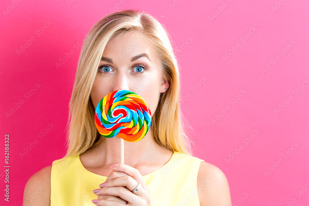 Young woman holding a lollipop on a pink background