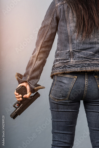 Woman in jeans is holding a gun in her hand with light effect.