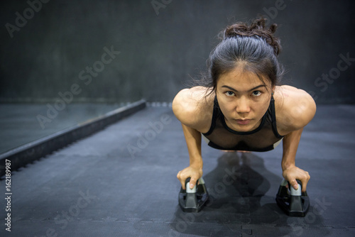 Young Asian athlete woman doing push up with push-up bars on the floor, sport and training in fitness gym concepts