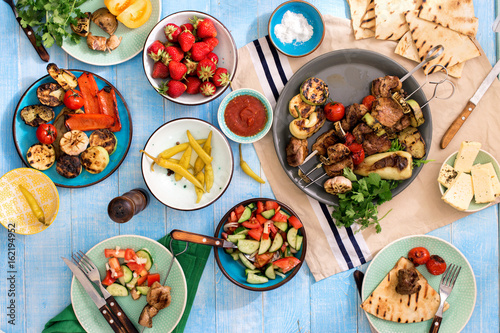 Dinner table with shish kebab, grilled vegetables, salad, snacks, strawberries