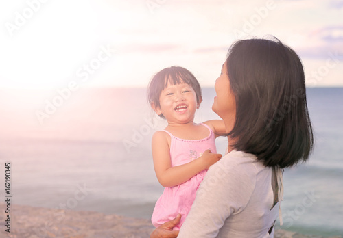 Happy loving family. Mother and her daughter child girl playing and hugging on beach background in the evening.