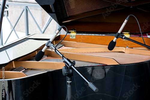 piano with raised lid. two microphones above the strings of black grand piano.