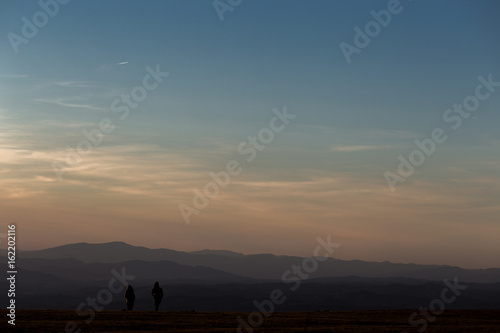 A boy and a girl on top of a mountain at sunset