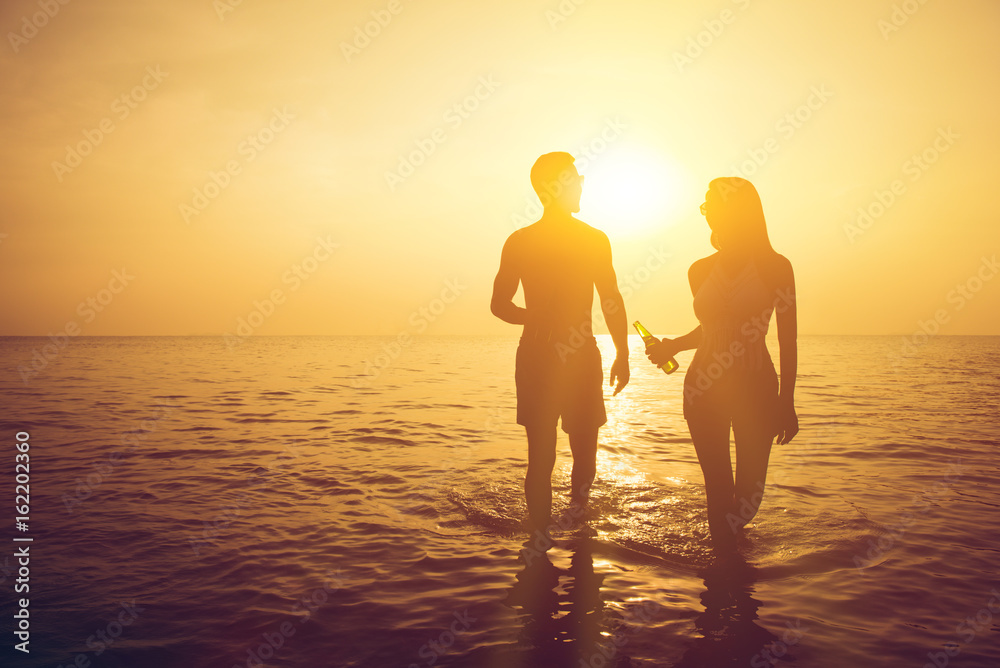 Silhouette of couple walking in seawater at the beach in sunset