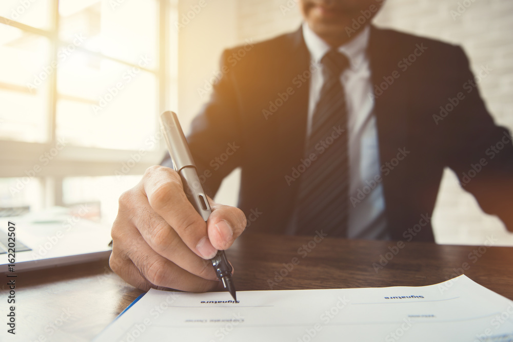 Businessman signing contract document at the table in the office Businessman signing contract document at the table in the office