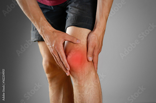 The guy clings to a bad knee. The pain in his leg. Closeup. The lesion is highlighted in red