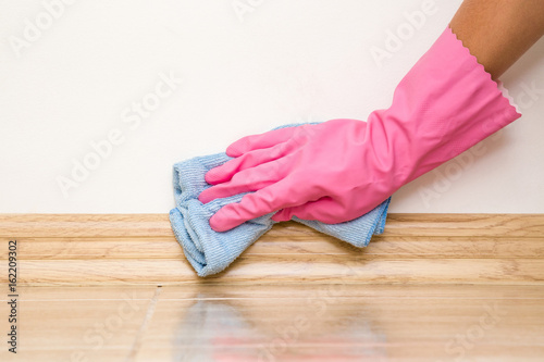 Hand in rubber protective glove cleaning baseboard on the floor from dust with rag at the wall. Early spring cleaning or regular clean up. Maid cleans house.