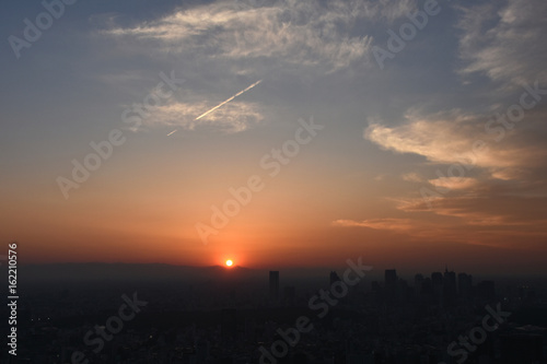 飛行機雲と沈む太陽・日本の東京都市景観（新宿の高層ビル群などを望む）
