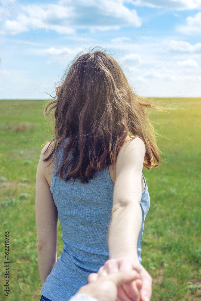 Follow me, Attractive brunette girl holding the hand of the leads in a clean green field, steppe with clouds Follow me, Attractive brunette girl holding the hand of the leads in a clean green field, steppe with clouds