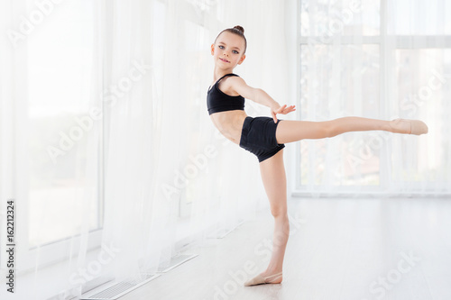 Flexible child, beautiful little gymnast girl doing gymnastic exercises or exercising in fitness class