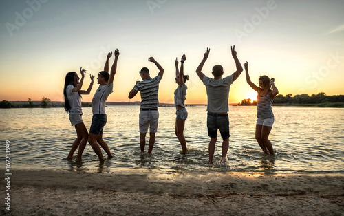 Silhouette of group young people on the beach under sunset sky w