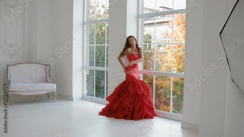 Gergeous woman in red dress posing in studio. Photographer work with model. Backstage. photo