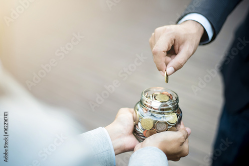 Businessman hand putting money (coin) in the glass jar held by a woman photo