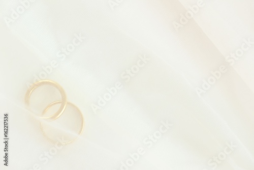 Closeup of two golden wedding rings under white wedding veil
