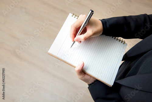 Woman writing on empty notebook with pen