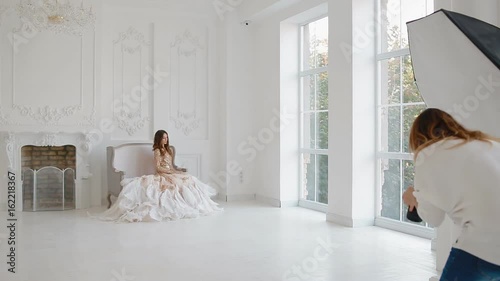 Gergeous woman in golden dress with ostrich feathers posing in studio. Photographer work with model. Backstage. photo