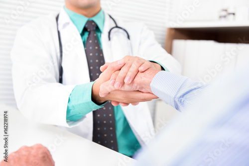 Doctor holding senior male patient hand with care
