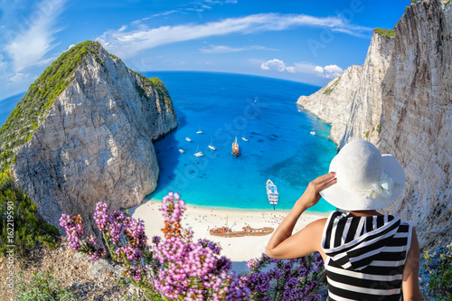Платно Woman with hat watching Navagio beach with shipwreck on Zakynthos island in Gree
