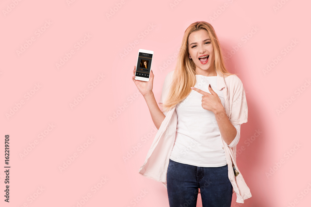 Young blonde girl is enthusiastic and points at her smartphone Young blonde girl is enthusiastic and points at her smartphone
