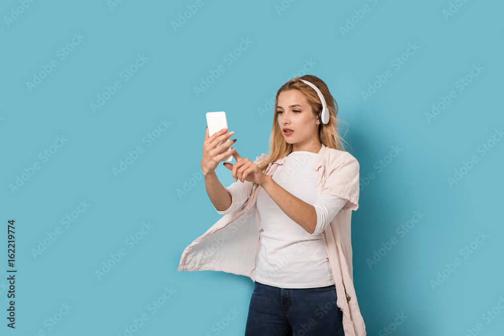 Young blonde with headphones is trying to pick the music on her smartphone Young blonde with headphones is trying to pick the music on her smartphone