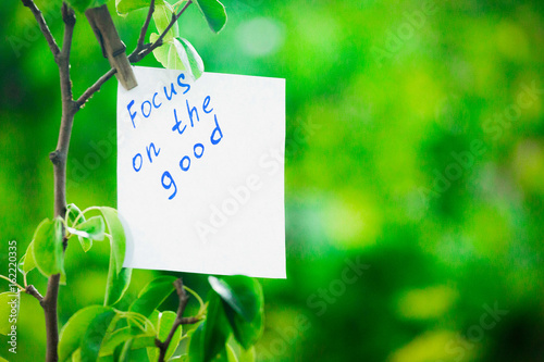 Motivating phrase focus on the good. On a green background on a branch is a white paper with a motivating phrase. photo