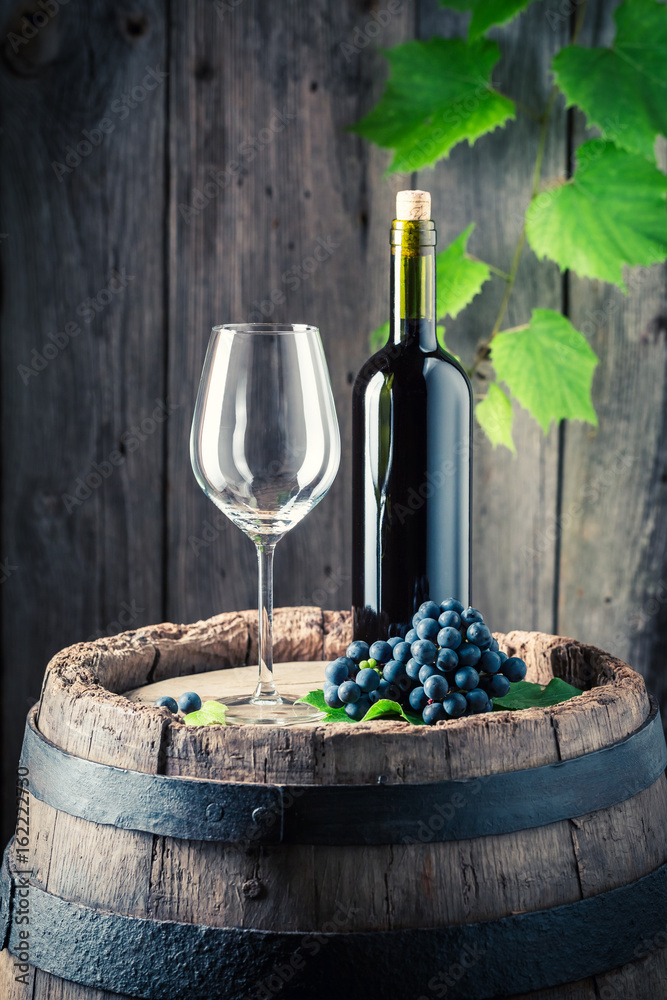 Red wine, empty glass and fresh grapes on old barrel