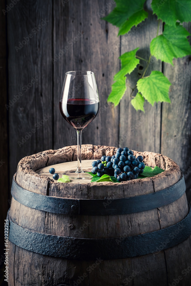 Glass of red wine and fresh grapes on old barrel