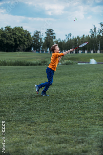 Caucasian boy playing badminton with racquet and shuttlecock, on green field