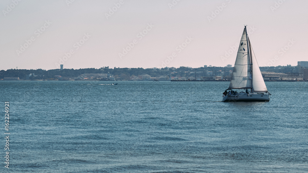 Sailing boat on the sea with urban coast on the background. Vaca