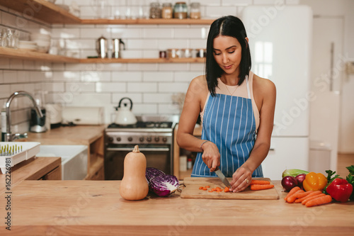 Foto Young woman cutting vegetables in kitchen at home