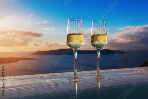 Two champagne glasses on the edge of infinity swimming pool at sunset on Santorini island