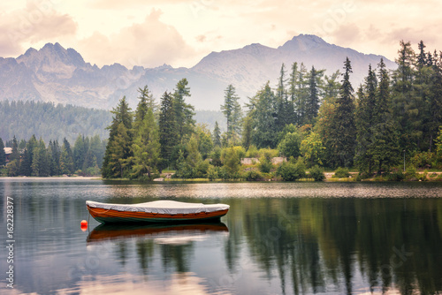 Beautiful alpine lake surrounded by rocky mountains with boat and green fir trees, popular tourist destination, lake Strbske pleso, High Tatras, Slovakia (Slovensko)