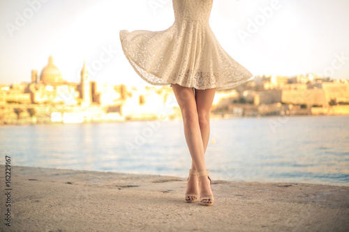 Details of woman's legs. She is wearing a white dress
