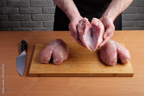 man in black apron holding chicken fillet in his hands, on background of cutting board
