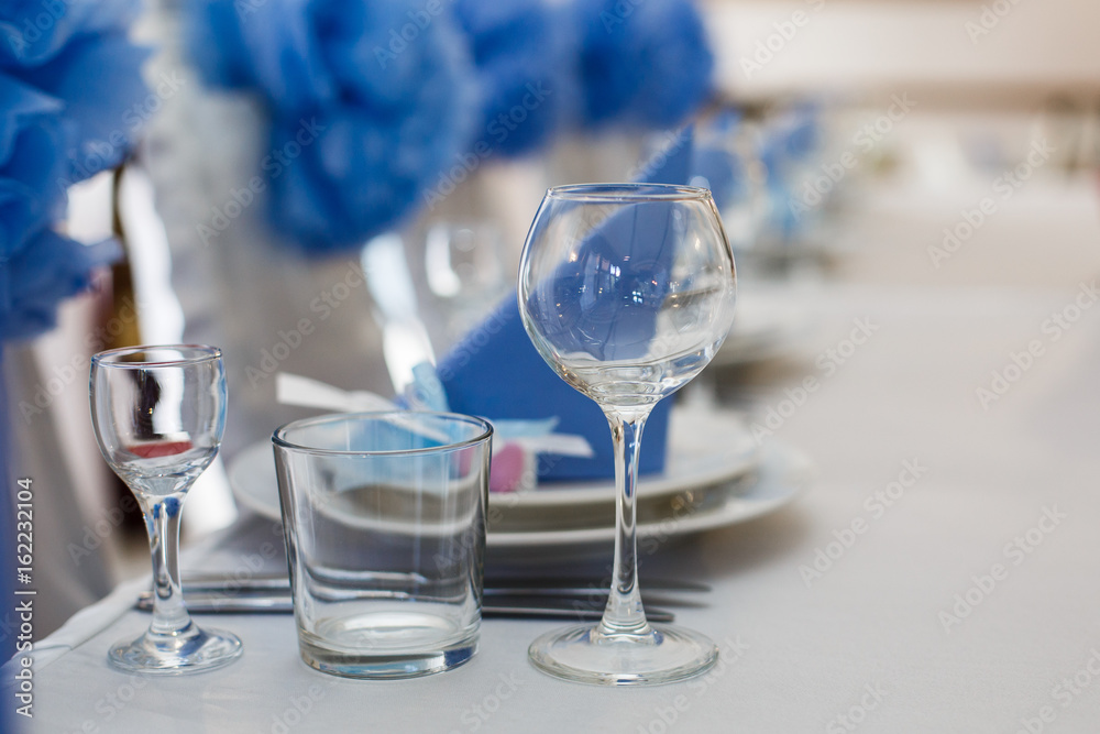 Empty glasses stand by dinner plates with blue serviettes