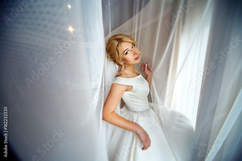 Curtain envelopes stunning bride while she stands before the window