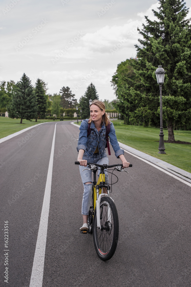 young smiling woman riding bicycle on asphalt road