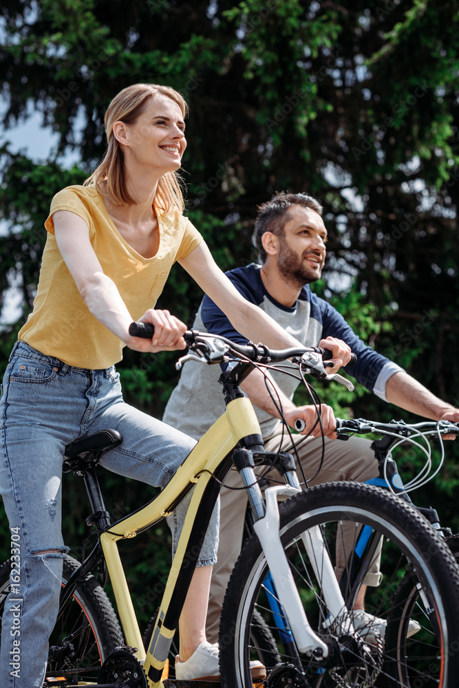 young smiling couple riding bicycles together at park