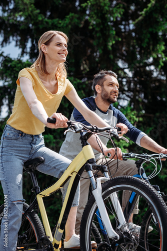 young smiling couple riding bicycles together at park
