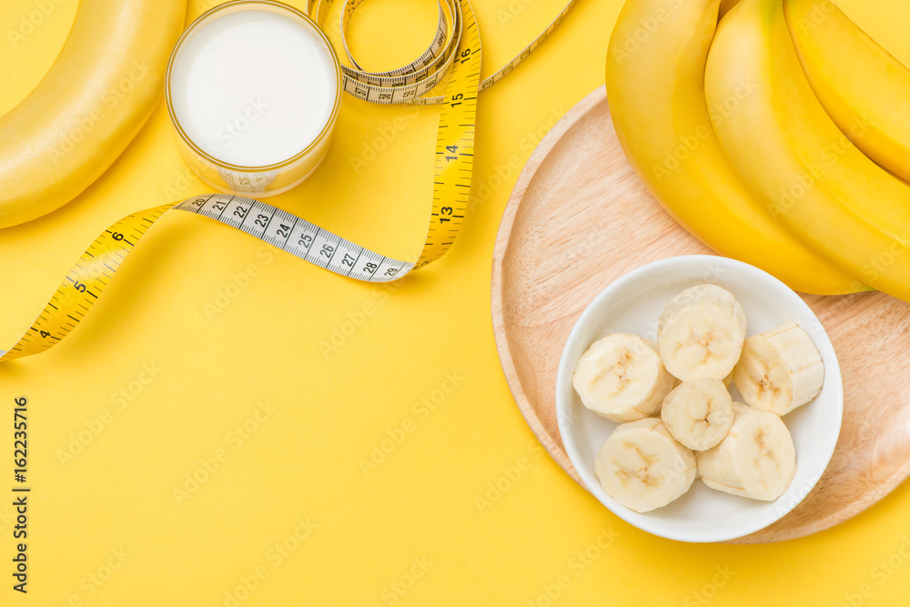Bananas and milk glass with measuring tape on yellow background with copy space