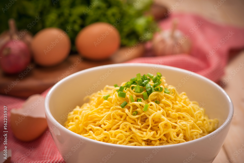 Instant noodles in bowl with vegetables on wood background Instant noodles in bowl with vegetables on wood background