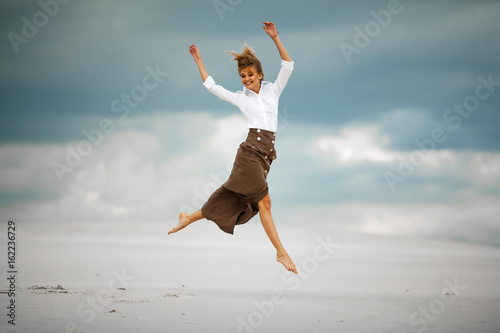 Young woman jumps on sand in desert and joyful laughs.