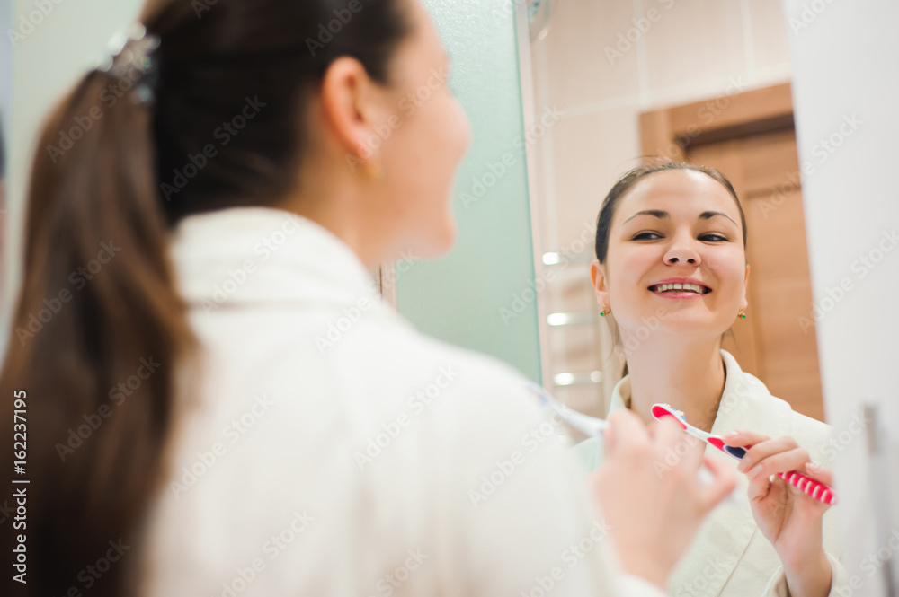 Image of pretty female brushing her teeth in front of mirror in the morning Image of pretty female brushing her teeth in front of mirror in the morning