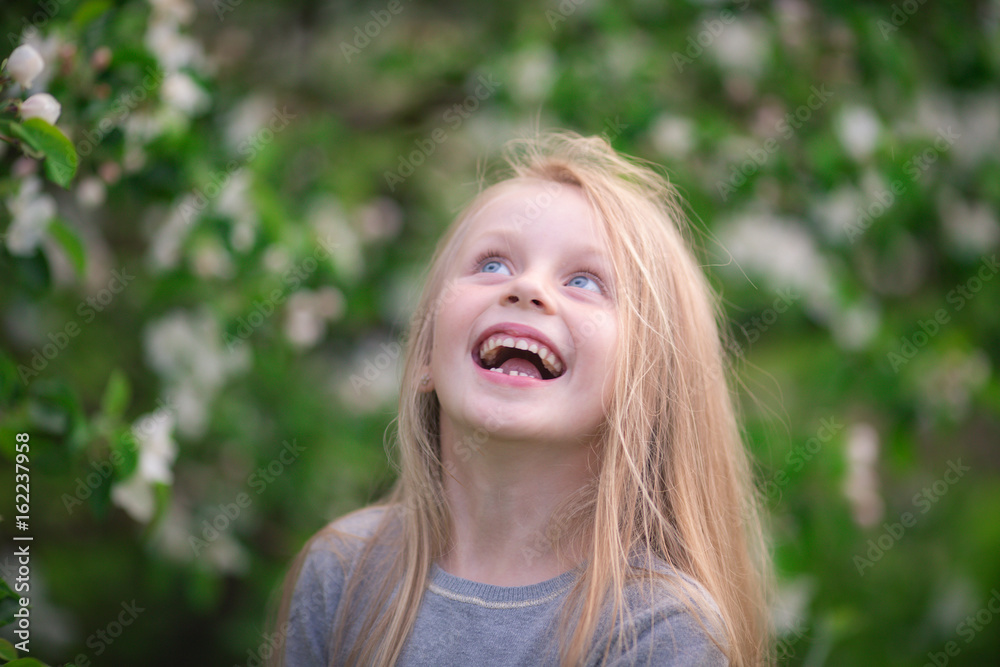A cute beautiful girl with long hair laughs next to a flowering tree in a park A cute beautiful girl with long hair laughs next to a flowering tree in a park