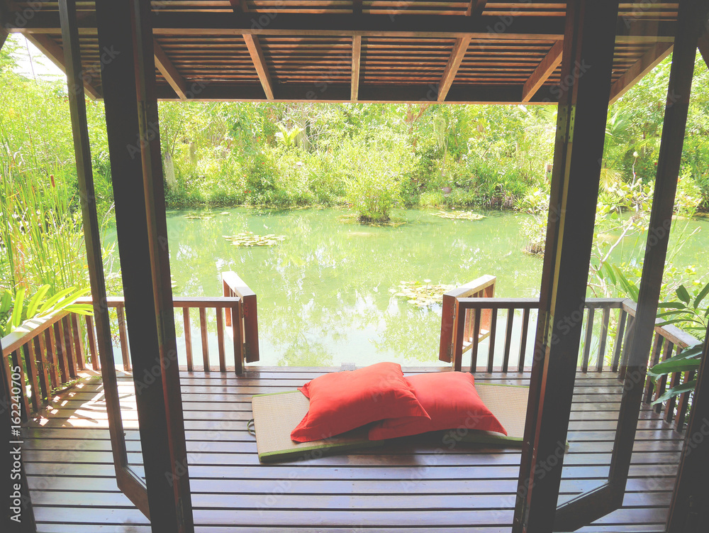 Wood patio on a relaxing green pond with bamboo floor mat and bright orange pillows