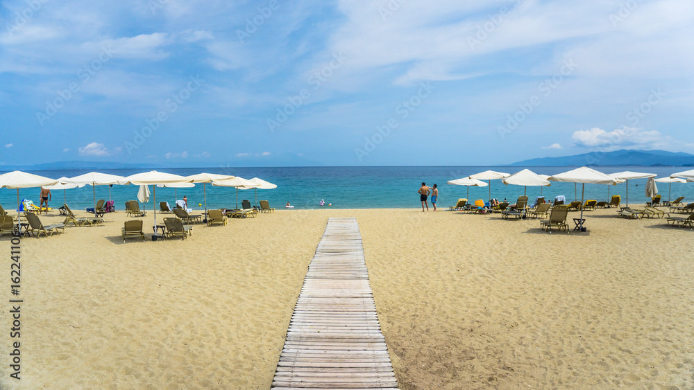 A wooden beach walkway between sun loungers and umbrellas. A wooden beach walkway between sun loungers and umbrellas.