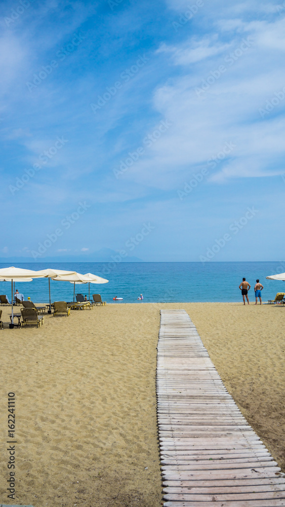 A wooden beach walkway between sun loungers and umbrellas.